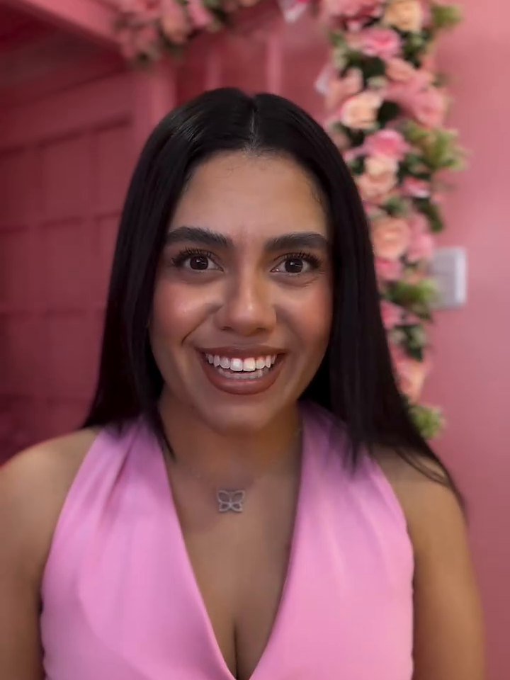 Giovanna Medeiros de colete rosa, sorrindo, no estúdio com flores